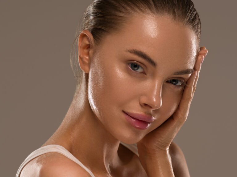 Imagen de una mujer bella sonriendo a la cámara mientras se toca el rostro, mostrando su piel radiante después de seguir la rutina de skincare recomendada por SkincareSelect.