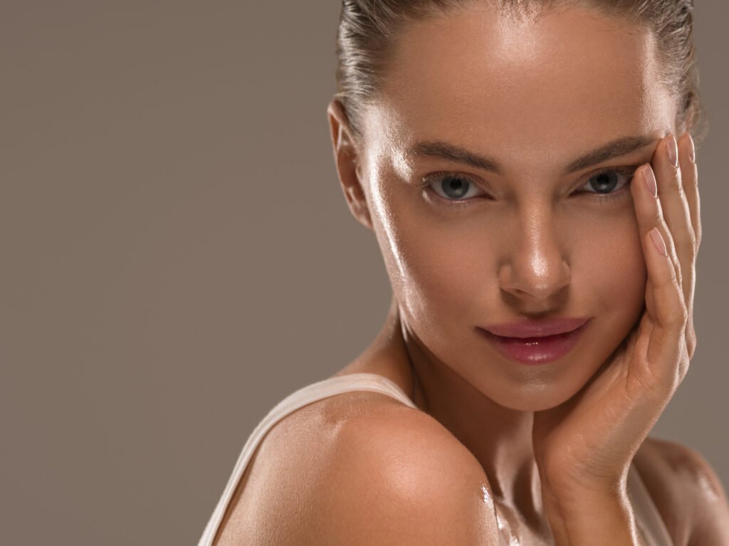 Imagen de una mujer bella sonriendo a la cámara mientras se toca el rostro, mostrando su piel radiante después de seguir la rutina de skincare recomendada por SkincareSelect.